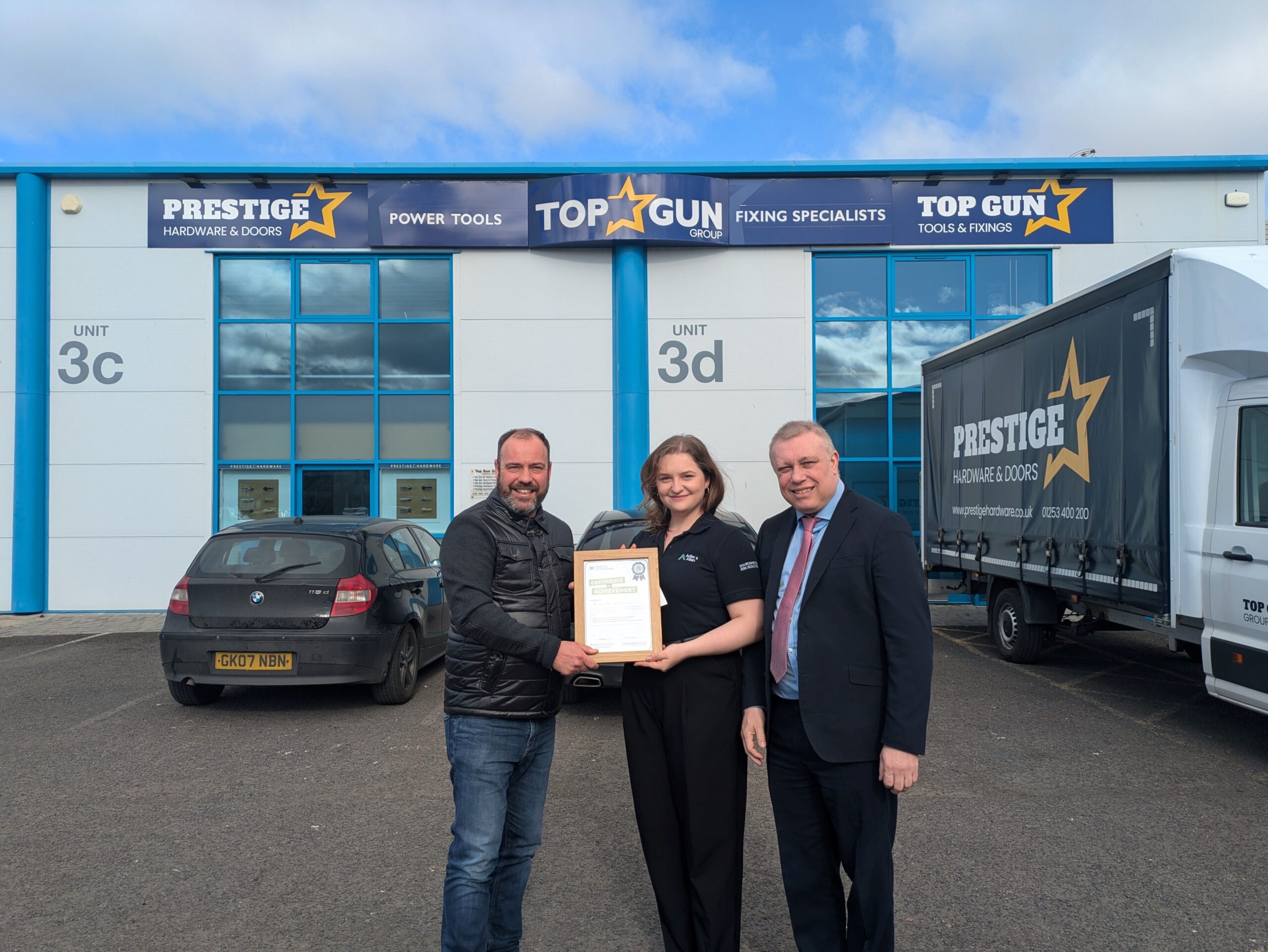 Three people stood Infront of a building holding a certificate