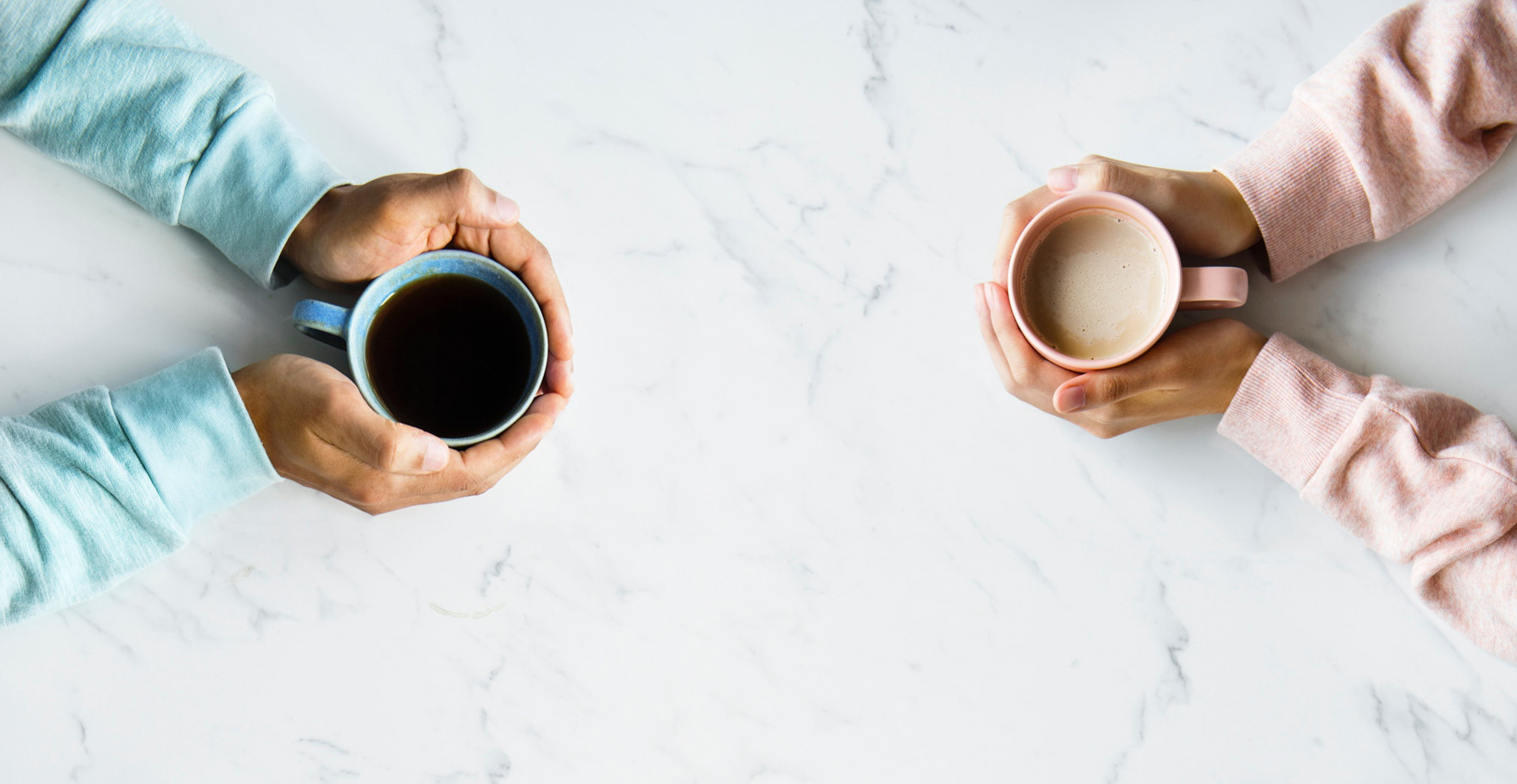 Hands of two people holding a hot drink facing each other.
